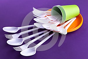 Bright orange and green set of disposable plastic tableware on purple background. Ecology problem. No plastic concept