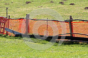 Bright orange makeshift improvised fence made of nylon net and wooden poles surrounded with uncut grass and molehills