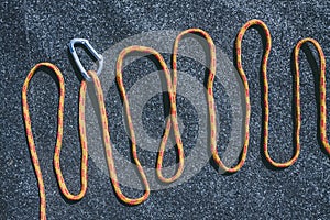 Bright orange rope with a small aluminum carabiner on a texured roofing felt surface with many small grey stones