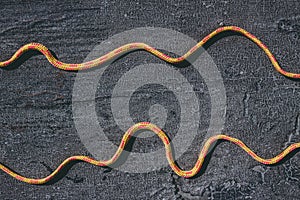 Bright orange rope on a texured roofing felt surface with many small cracks