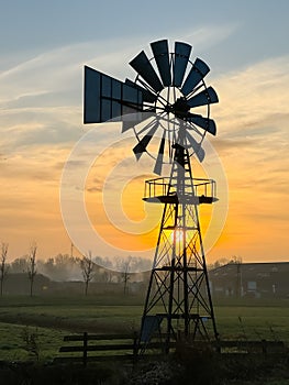 Bright orange sunrise at fields with light fog and an American style windmill