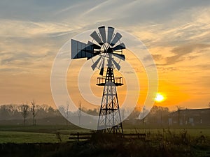 Bright orange sunrise at fields with light fog and an American style windmill