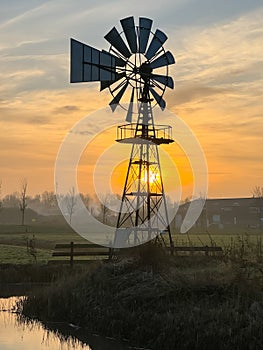 Bright orange sunrise at fields with light fog and an American style windmill