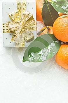 Bright orange tangerines on branches with green leaves gift box in silver paper golden ribbon with bow snow. Christmas New Year