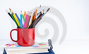 Bright pencils in a red mug on the books on the desk. Back to school. Banner. Place for text. Selective focus