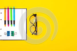 Bright pens, glasses and notebook lie isolated on yellow background