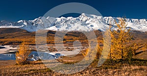 Bright picturesque autumn landscape with mountains covered with snow, forest, yellow larches and beautiful lake with reflections photo