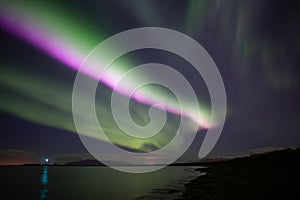 Bright pink aurora borealis over ocen, Grotta lighthouse Iceland