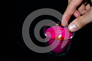 Bright pink candle in a glass jar on a black background. The candle is burning. Redeemed. A hand sets fire to a candle with