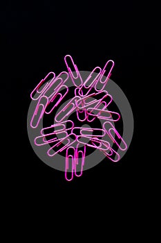 Bright pink paperclips on a black background