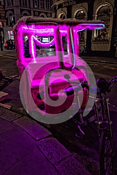 Bright pink pedicab, illuminated by rope lights. Shaftesbury Avenue, London.