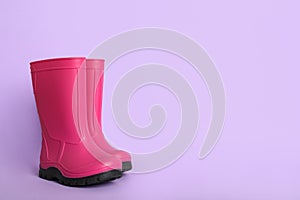 Bright pink rubber boots on violet background. Space for text