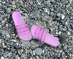 Bright pink slippers are on the pebble beach. Summer walk, sea tourism