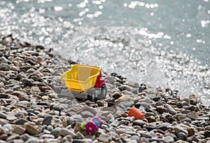 Bright plastic baby toy cars on a pebble beach near the sea. Waiting for summer