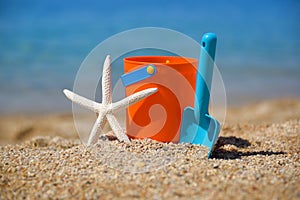 Bright plastic children`s beach toys and a starfish on sand near sea.