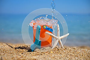 Bright plastic children`s beach toys and a starfish on sand near sea. Summer vacation concept