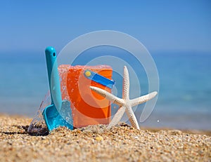 Bright plastic children`s beach toys and a starfish on sand near sea. Vacation concept