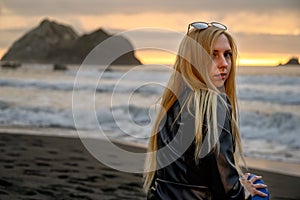 Bright portrait of an attractive blonde woman smiling conservatively by the ocean somewhere at the shores of Northern California