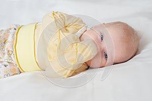 Bright portrait of cute baby with fingers in mouth in white bed