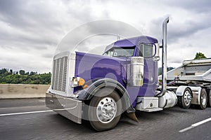 Bright purple classic big rig semi truck with chrome accessories transporting cargo in tip semi trailer for carry heavy freights