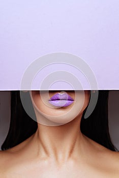 Bright purple lips looks into the hole of the colored paper.