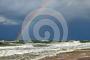 Bright rainbow on the background of storm clouds over the raging sea