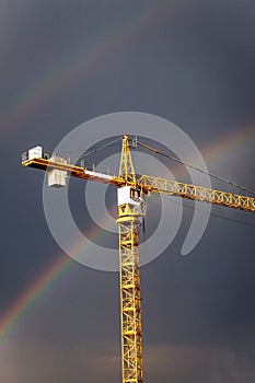 A bright rainbow in the dark gray sky and yellow crane