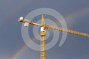 A bright rainbow in the gray sky and yellow crane