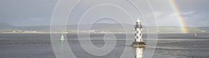 Bright rainbow high in sky over lighthouse in sea during dark storm