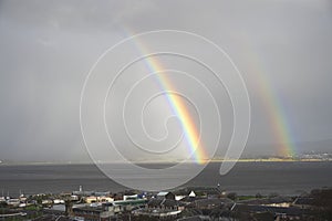 Bright rainbow high in sky over the sea during dark storm