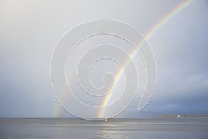 Bright rainbow high in sky over sea during dark storm