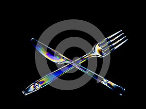 Bright rainbow stress patterns show in transparent plastic cutlery. Polarised light on a dark background.