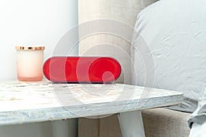 Bright red alarm clock and candle jar on a bedside table nightstand, with bed and linens showing in soft colors