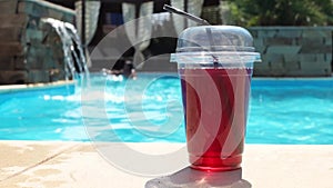 Bright red alcohol cocktail in a disposable plastic cup with straw by the pool