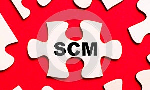 On a bright red background, white puzzles. In one of the pieces of the puzzle, the text SCM Supply Chain Management