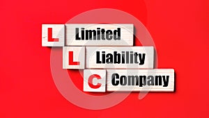 On a bright red background, wooden cubes and blocks with the text LLC Limited Liability Company. Manufacturing of wooden toys