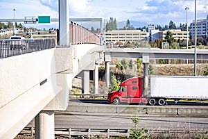 Bright red big red semi truck with dry van semi trailer running on the highway intersection with overpass road and bridge with