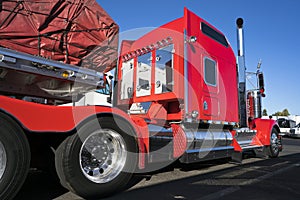 Bright red big rig classic American semi truck with flat bed semi trailer carry commercial cargo covered and fixed by slings stan