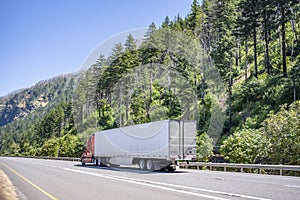 Bright red big rig industrial semi truck with refrigerator semi trailer transporting cargo running on the gorgeous highway road on