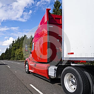 Bright red big rig long haul semi truck with high cabin transporting cargo in semi trailer driving on multiline road