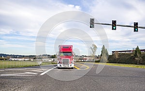 Bright red big rig powerful semi truck with grille guard driving on the road standing on crossroad intersection waiting for green