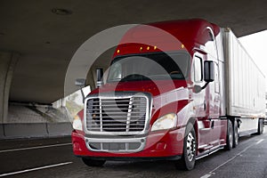 Bright red big rig semi truck with dry van trailer driving on hi