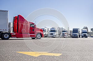 Bright red big rig semi truck with extended cab transporting cargo in dry van semi trailer driving on the truck stop parking lot