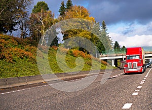 Bright red big rig semi truck transporting container on flat bed