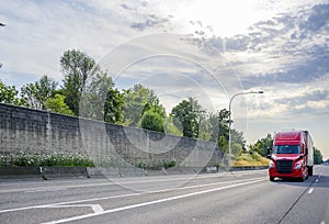 Bright red big rig semi truck transporting goods in dry van semi trailer running on the straight wide highway road with concrete