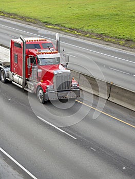 Bright Red Classic Big Rig Semi Truck with Chrome Accessories Running with Flat Bed Semi Trailer on the Divided Highway Road
