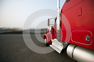 Bright red classic big rig semi truck with chrome pipe and filter running on the wide road