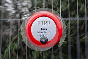 Bright red fire alarm bell turn handle spin around to operate alert manual steel ringing on construction building site