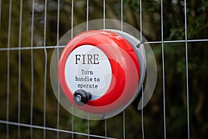 Bright red fire alarm bell turn handle spin around to operate alert manual steel ringing on construction building site