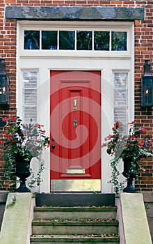 A bright red front door with cream trim and a transom with front steps on a red brick house building